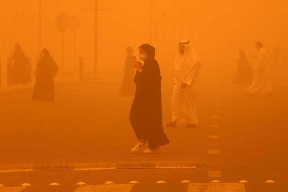 Pedestrians cross a road amid a severe dust storm in Kuwait City on 23 May 2022