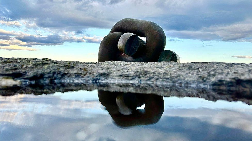 Two giant chain links on a rock reflected in a puddle