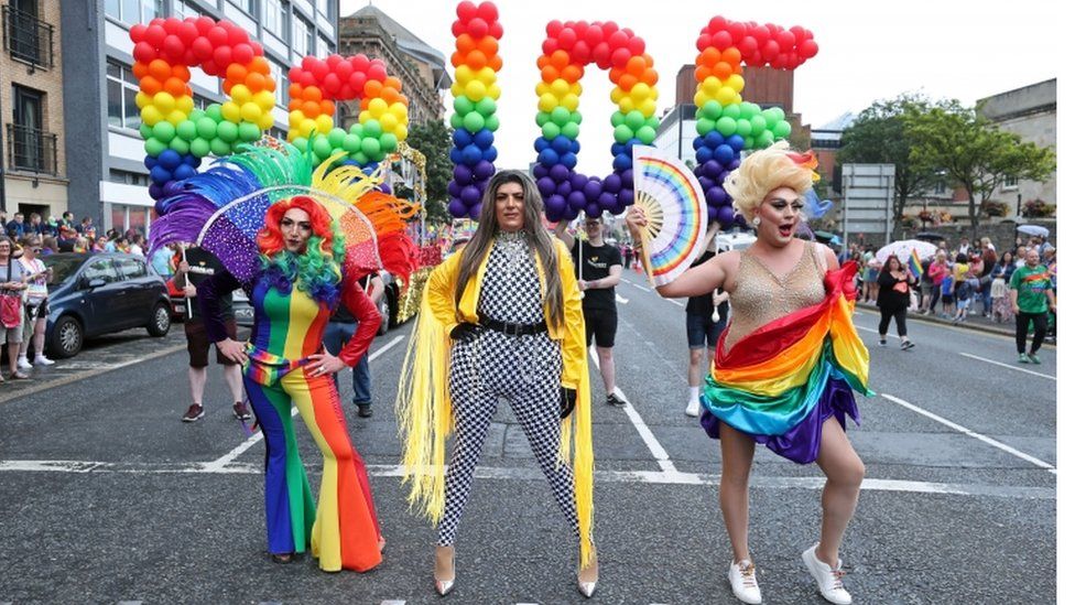 Drag queens stand in front of pride balloons