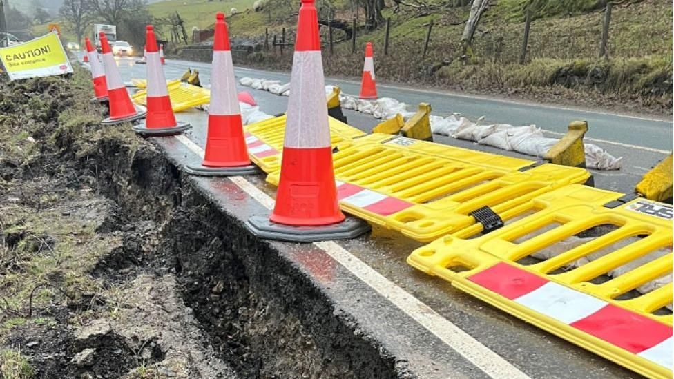 The closed A59 with traffic cones, showing the cracked road verge