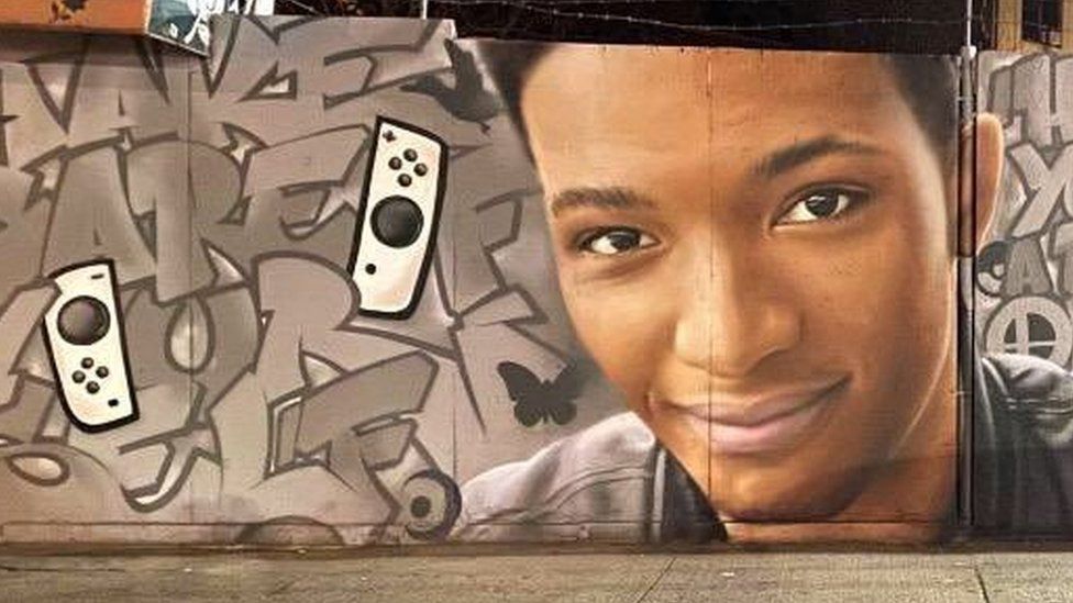 A mural on a wall in New York City. It is graffiti with the face of Etika, a young male. Beside him are two Nintendo Switch controllers