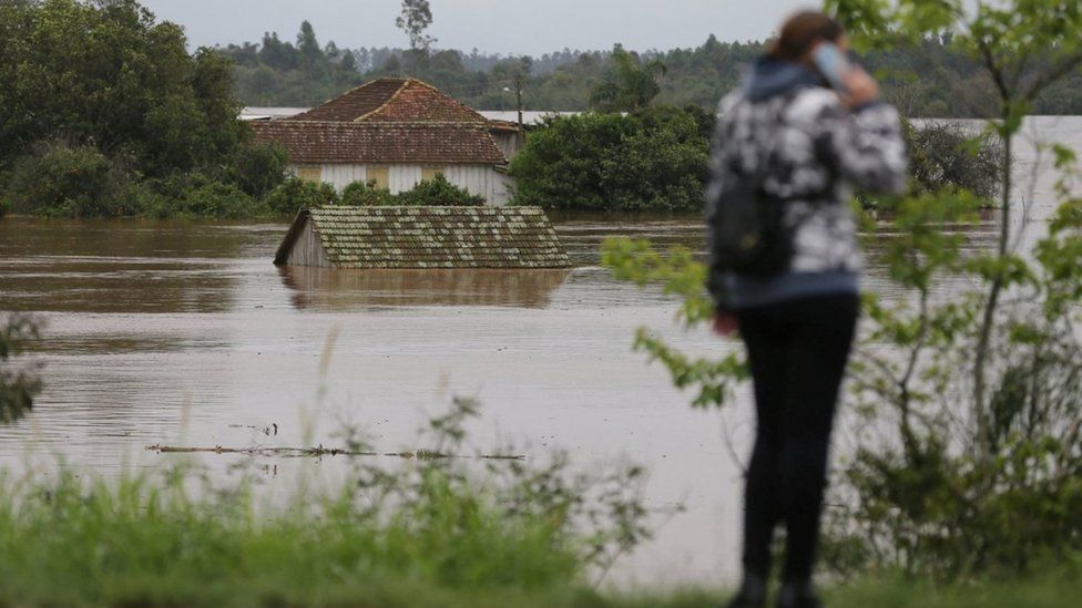 A woman stands in front of a flooded house after a cyclone hit southern towns, in Bom Retiro do Sul, Rio Grande do Sul state