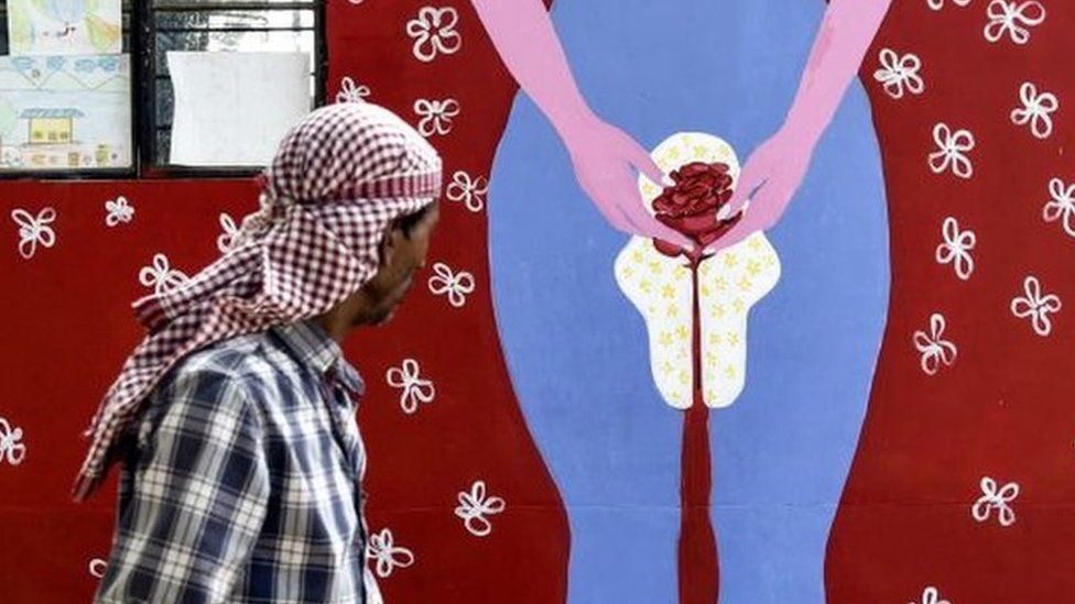 An Indian man looks on as he walks along a wall painting about menstruation in Guwahati on May 28, 2019