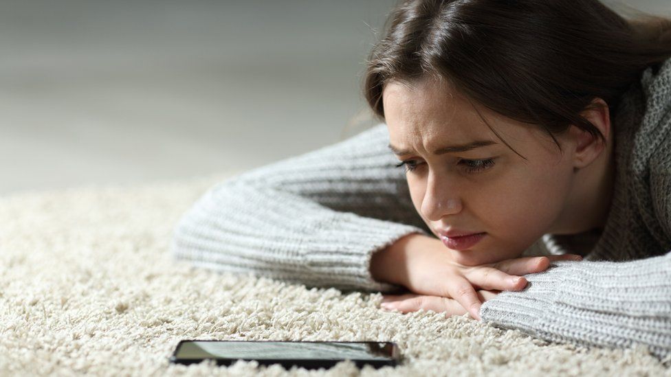A young woman lying on the floor looking at her smartphone with concern