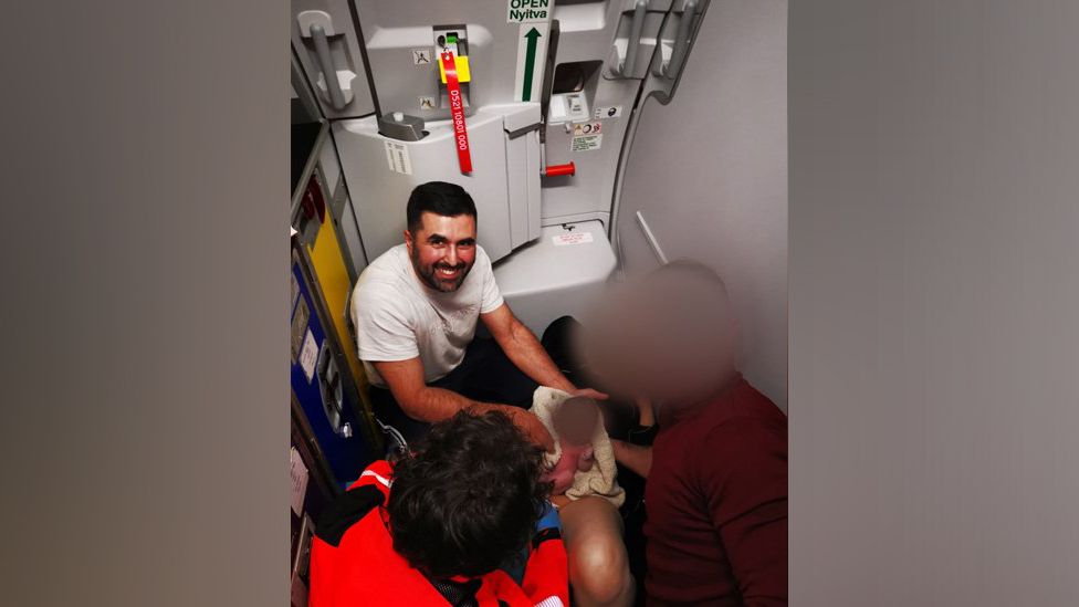 Hassan Khan poses with the baby and her mother, whose faces have been blurred, on the plane