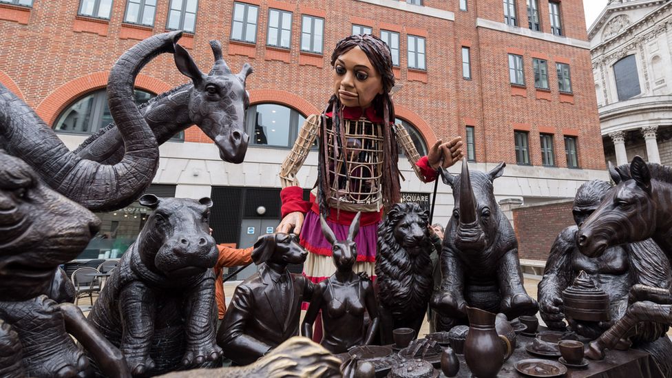Little Amal stood with a statue of various animals