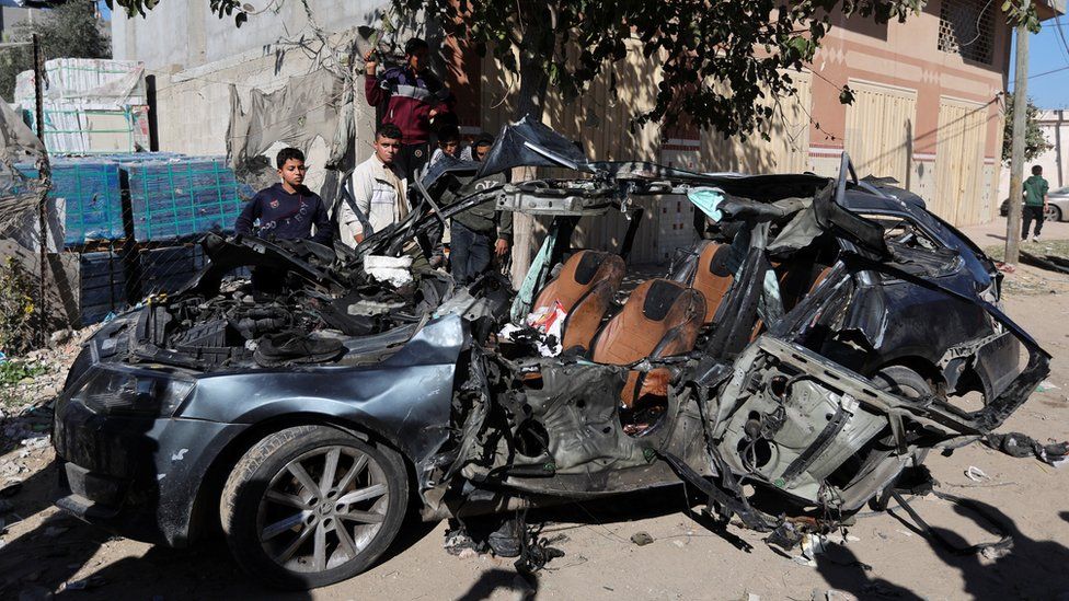 Palestinians inspect the wreck of a car destroyed in an Israeli air strike that killed , in the city of Rafah, in the southern Gaza Strip (7 January 2024)