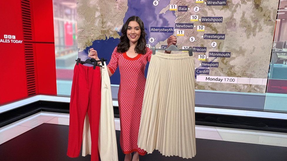 Sabrina holding up some of her clothes in the TV studio in front of a weather map