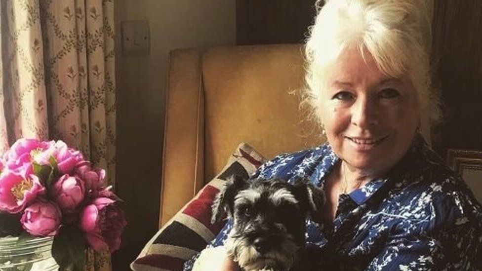 Debbie Matthews sitting on an armchair with her dog, which has black and white fur