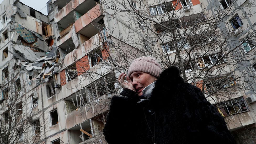 A woman stands outside a damaged block of flats in Mariupol, Ukrainec, 17 March 2022