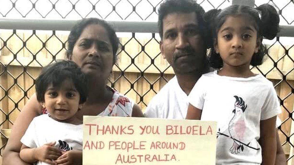A family picture of Nadesalingam and Priya and their two daughters holding a sign reading "thanks you Biloela and people around Australia"