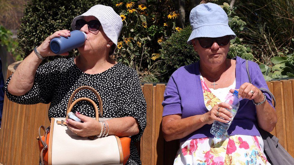 Women rest on a bench and drink water in hot weather in Canary Wharf in London on Friday