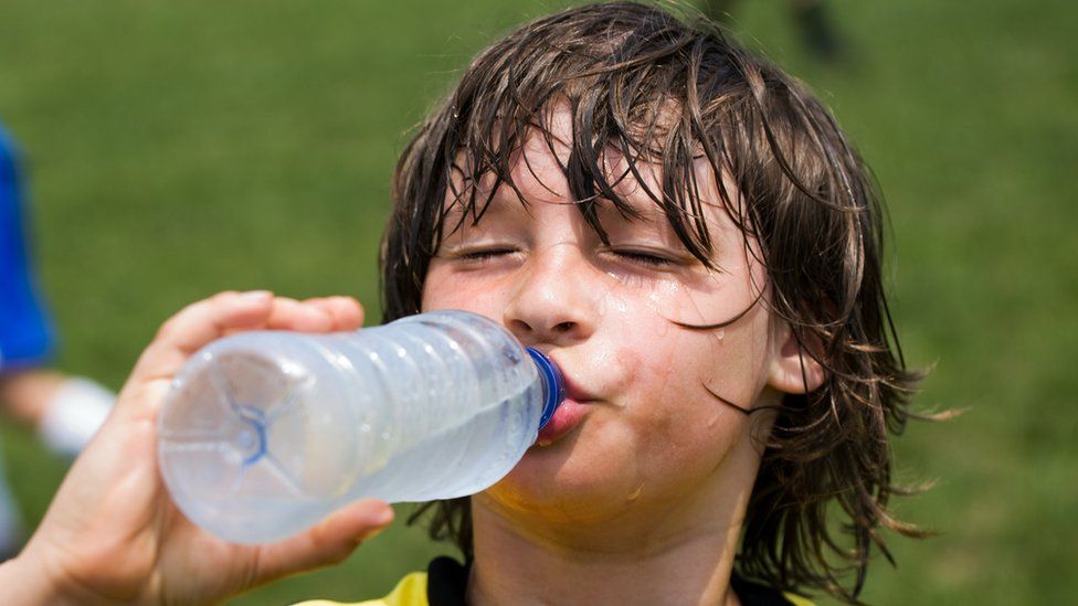 Boy playing football drinking from a water bottle