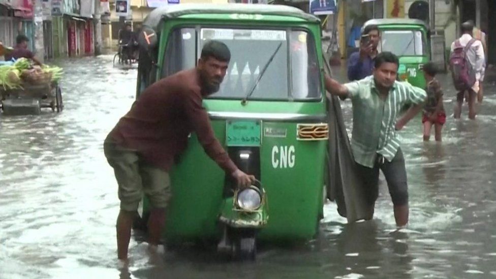 Two men push tuk tuk through flooded streets in Bangladesh