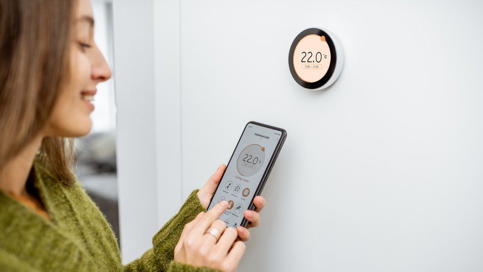 A woman interacts with the Google Nest smart thermostat on a wall