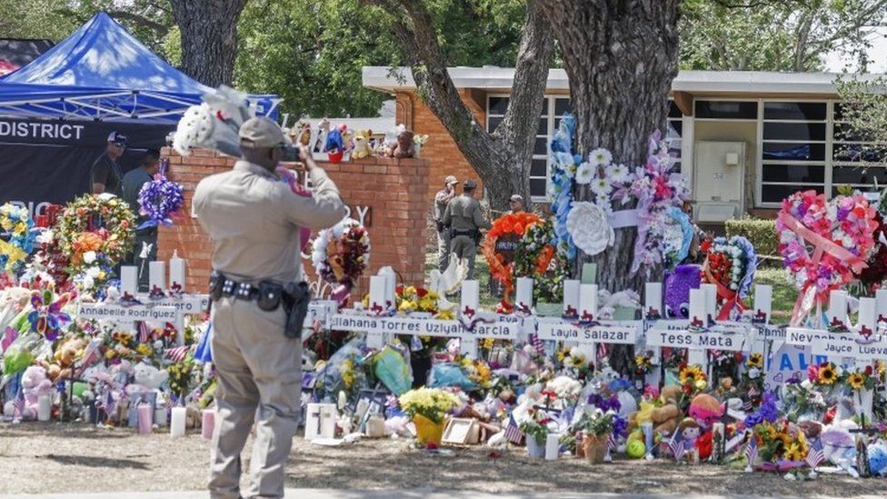 A Texas Highway Patrol officer takes cell phone pictures of the memorial to the victims following the mass shooting at the Robb Elementary School in Uvalde, Texas