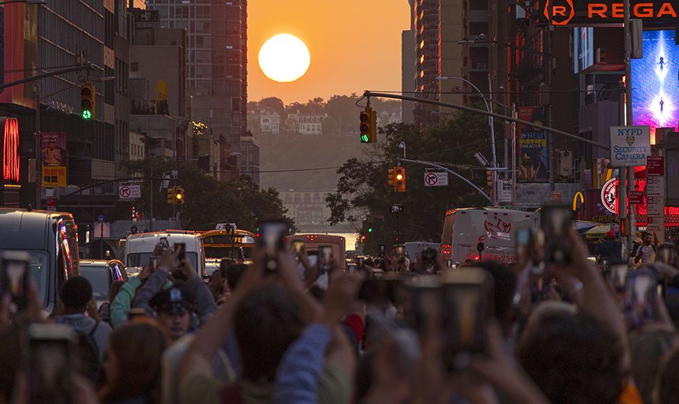 People stand on 42nd Street in Times Square as they photograph the second evening of the Manhattanhenge sunset on May 30, 2023