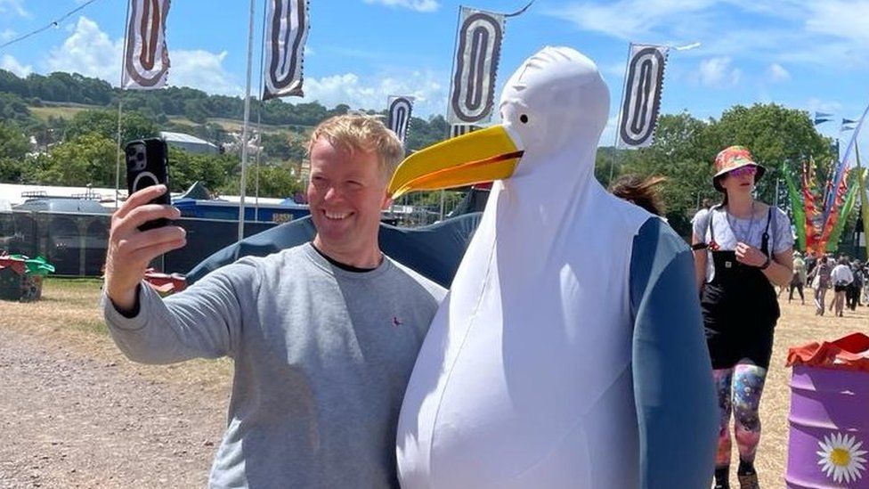 Gareth Turnbull takes a selfie with a person dressed as a penguin at Glastonbury