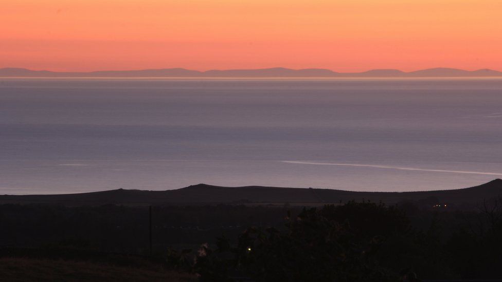 Llun maint llawn: Mynyddoedd Wicklow a'r tonnau'n torri ar draeth Dinas Dinlle o'r Groeslon