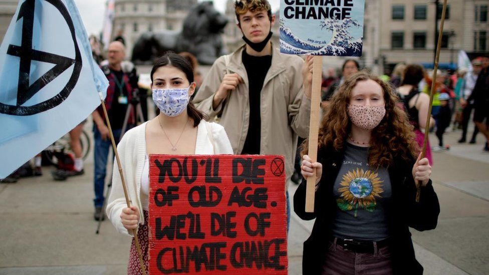 Three young XR activists holding a sign saying "you'll die of old age, we'll die of climate change"