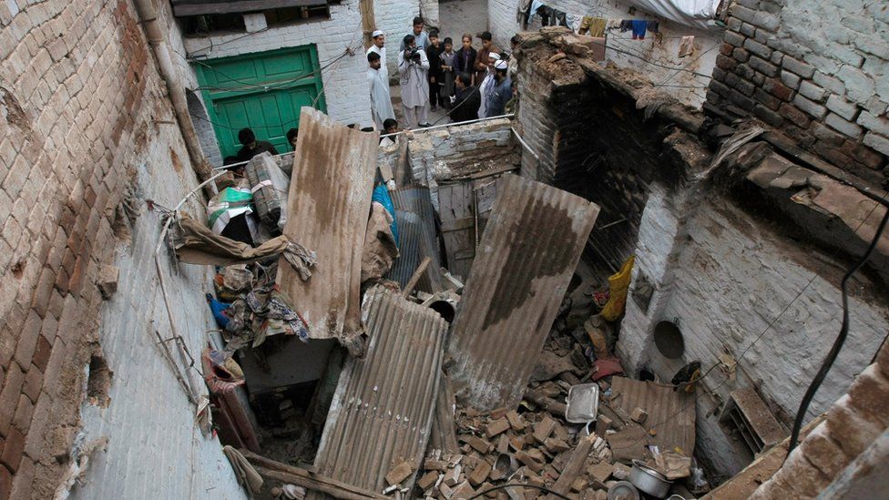 People stand outside a house damaged by an earthquake in Peshawar, Pakistan (26 Oct. 2015)