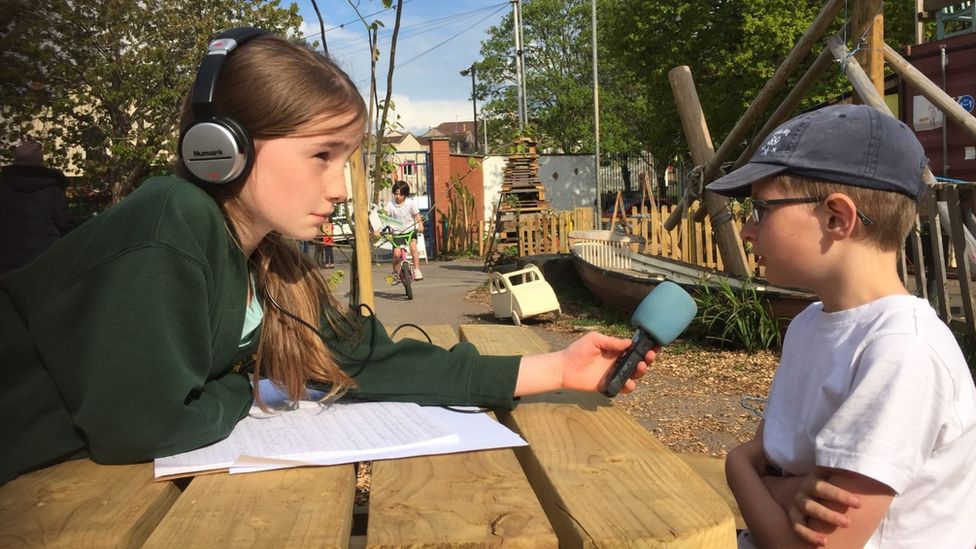 Two children sat at a picnic bench recording a podcast