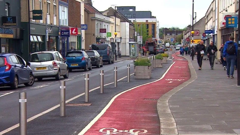 Image of the cycle lane on Keynsham High Street. It is painted bright red, with bollards to the left.