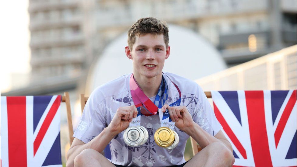 Man holding Olympic medal crouched down behind the Union Jack flag