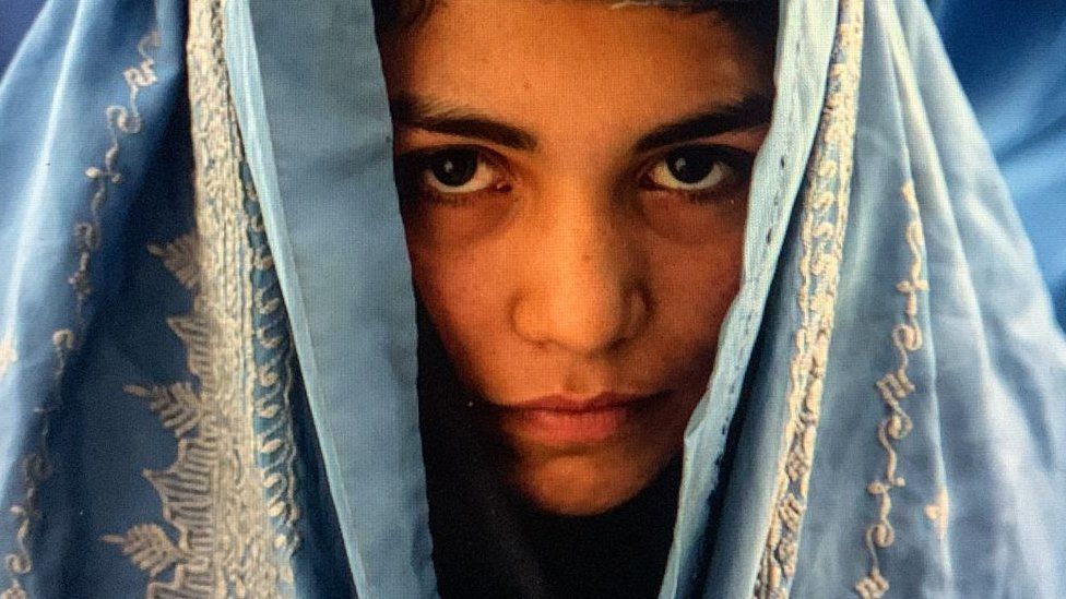 A young woman waiting outside a bakery shop to receive donated bread, June 2022, Kabul