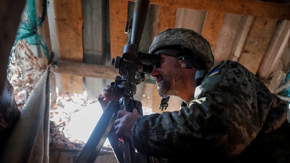 A Ukrainian service member uses a periscope while observing the area at a position on the front line near the village of Travneve in Donetsk region