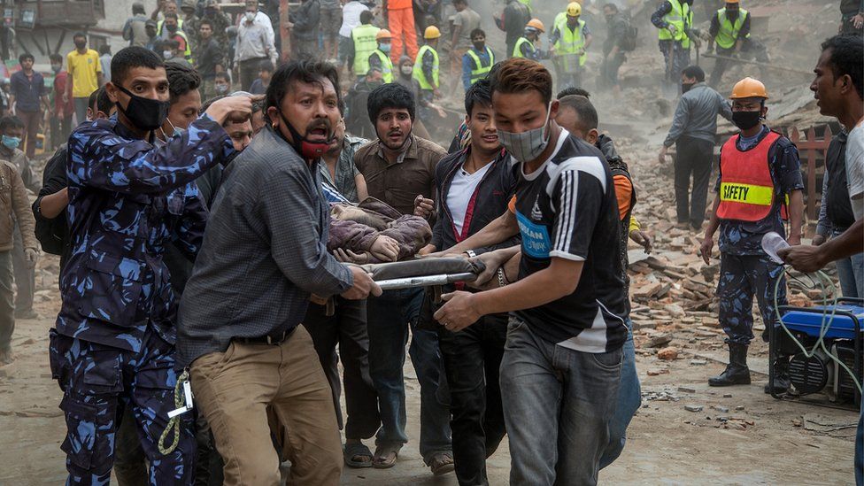 Men carrying a stretcher with rubble in the background