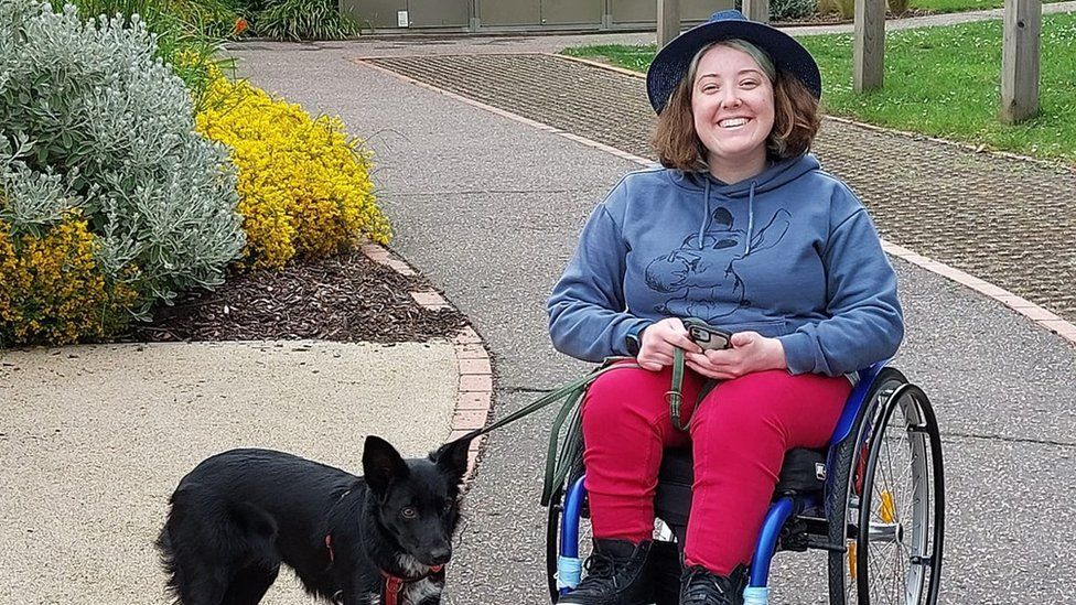 Lucy King in her wheelchair with a black dog on a lead next to her