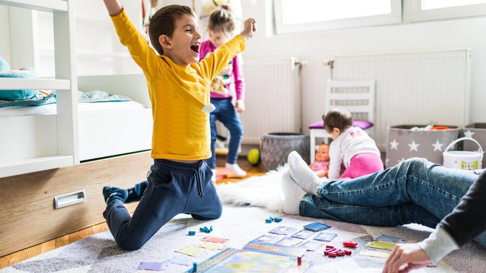 kid celebrating a win playing a board game with an adult while other kids play in the background