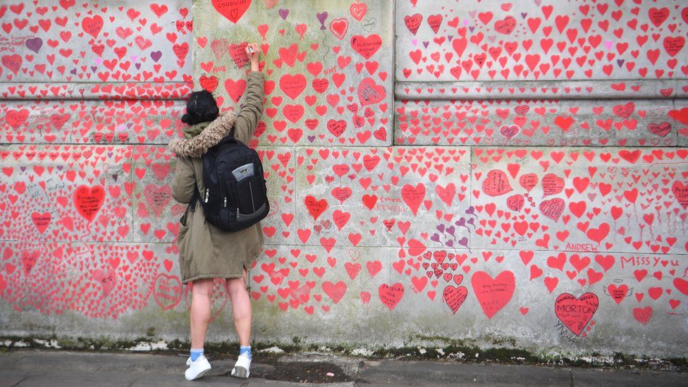 A person writes in a heart on the National Covid Memorial Wall on the Embankment in London