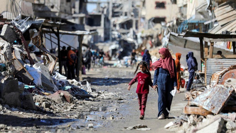 Palestinians walk past destroyed buildings in Gaza City (20 March 2024)