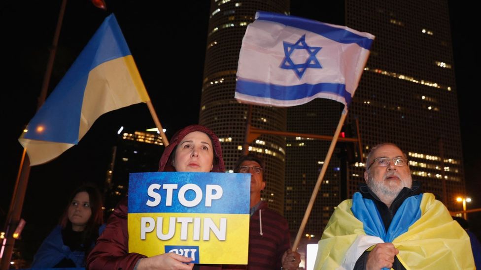 A middle-aged woman and a grey-bearded man wave Ukrainian and Israeli flags during a protest against Russia's military invasion of Ukraine, in Israel's Mediterranean coastal city of Tel Aviv on March 12, 2022