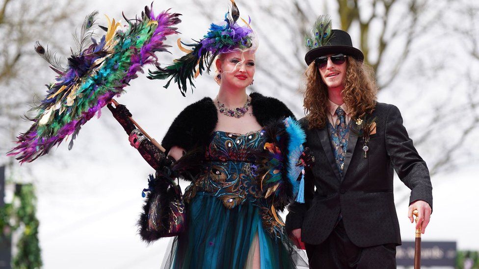 Woman holding parasol and man wearing a hat at Aintree Ladies Day 2024
