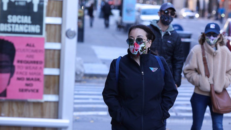 Pedestrians walk past a store with guidelines for social distance and face masks
