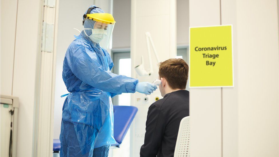 A nurse in protective wear taking a temperature