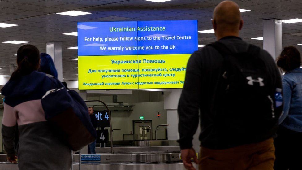 People walk past an information billboard at London Luton Airport designed for Ukrainian refugees who arrive in the United Kingdom