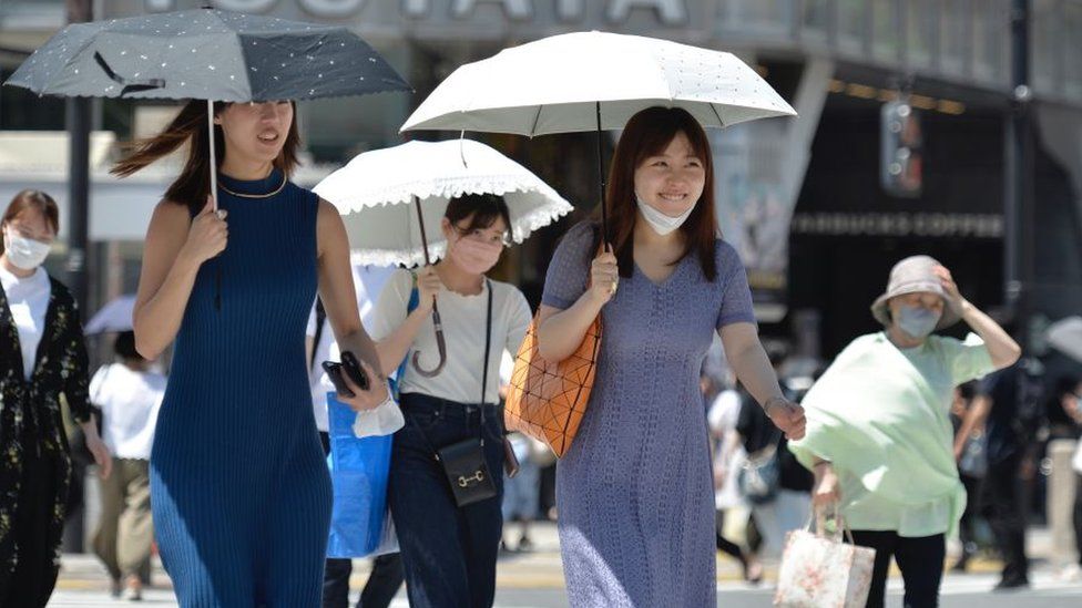 People walk on the street using an umbrella to protect themselves from the sun on June 27, 2022, in Tokyo's popular Shibuya district in Tokyo, Japan.