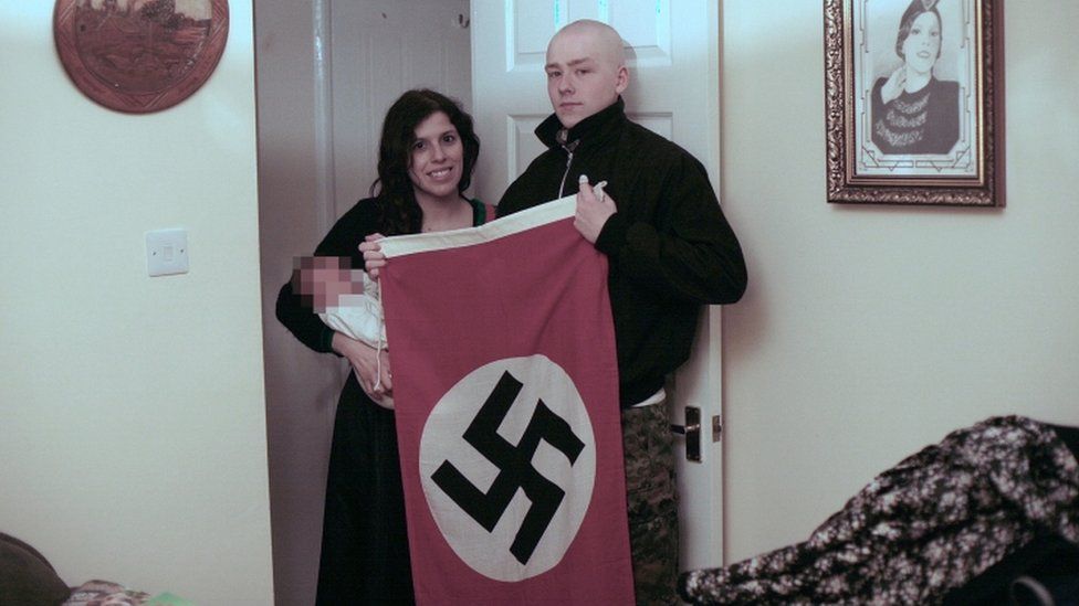 Claudia Patatas and Adam Thomas, holding their baby and a Swastika flag