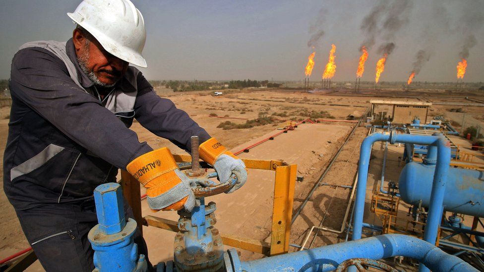 An Iraqi oil technician turns a valve at a gas installation as flames resulting from the burning of excess hydrocarbons rise in the background at the Nahr Bin Omar natural gas field, north of the southern Iraqi port of Basra