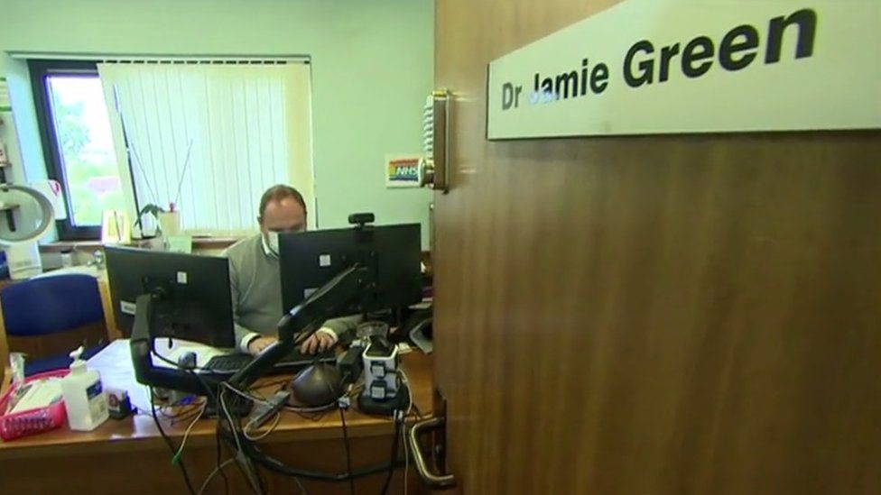 Dr Jamie Green sitting at a desk in his consulting room