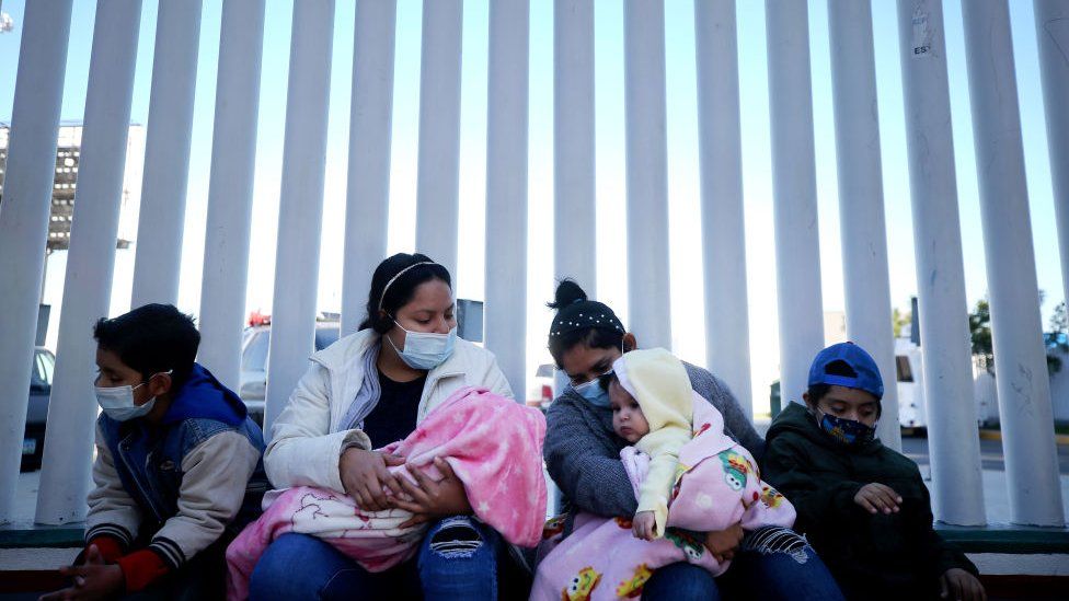 El Salvador and Honduras nationals seeking asylum in the United States sit outside the El Chaparral border crossing on February 19, 2021 in Tijuana, Mexico