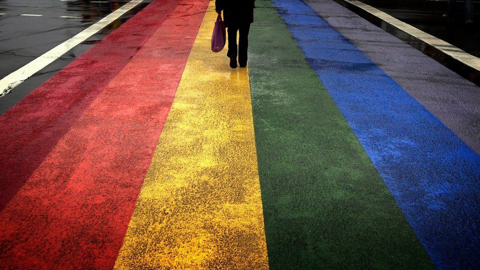 A figure walks along a rainbow painted road