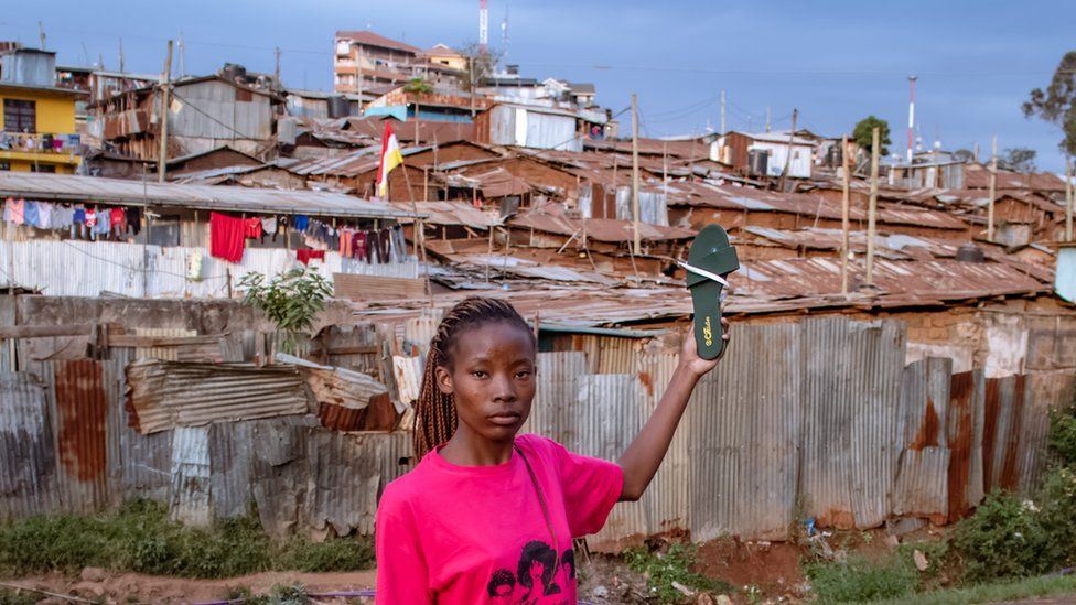 Diana Mwazi standing in front of shacks in Kibera