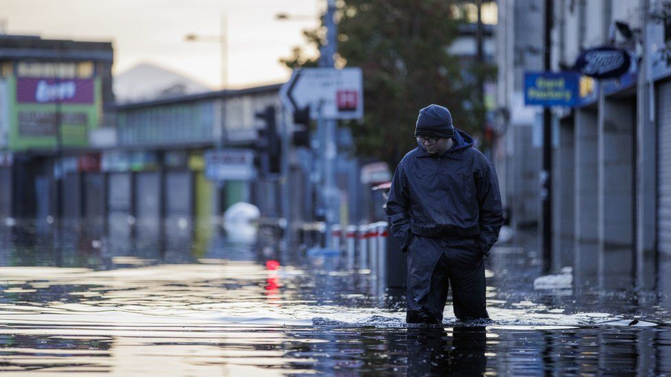 A man in waterproofs walks through knee-high floodwater in Downpatrick