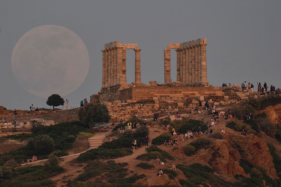 Locals and tourists watch the moon rising by the Temple of Poseidon at the cape of Sounion, south of Athens, Greece