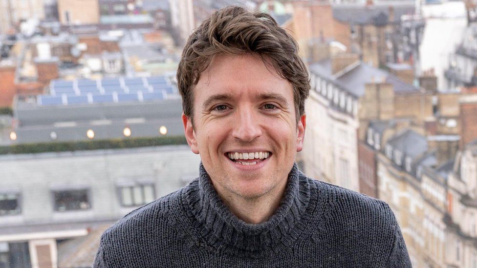 Greg James smiling with London behind him